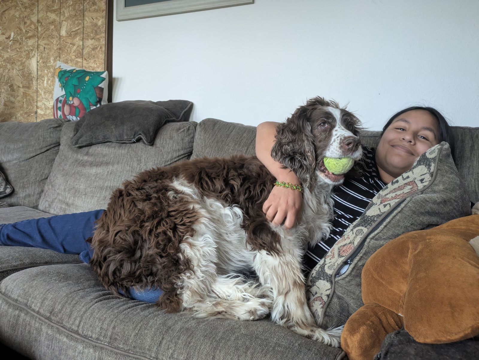 Feliz on the couch with her arm around Maggie, who has a tennis ball in her mouth.